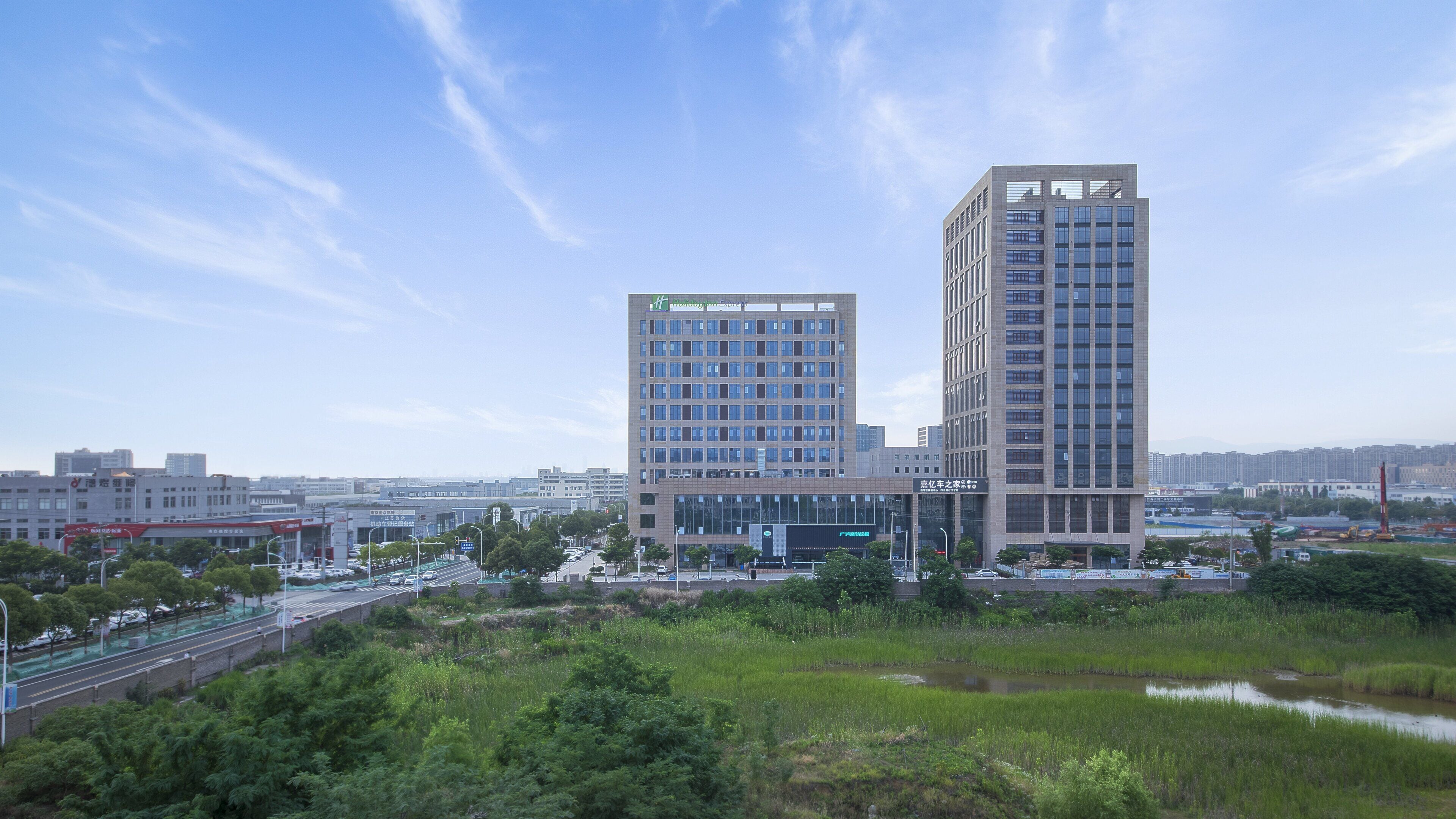 A modern high-rise building with multiple floors, surrounded by greenery and a clear sky.
