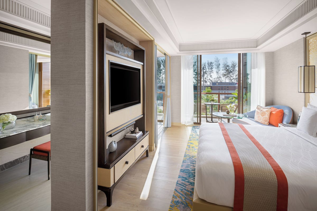 Een hotelkamer met een groot bed, een televisie bevestigd aan een houten kast, een bureau met een stoel, en uitzicht buiten door grote ramen.