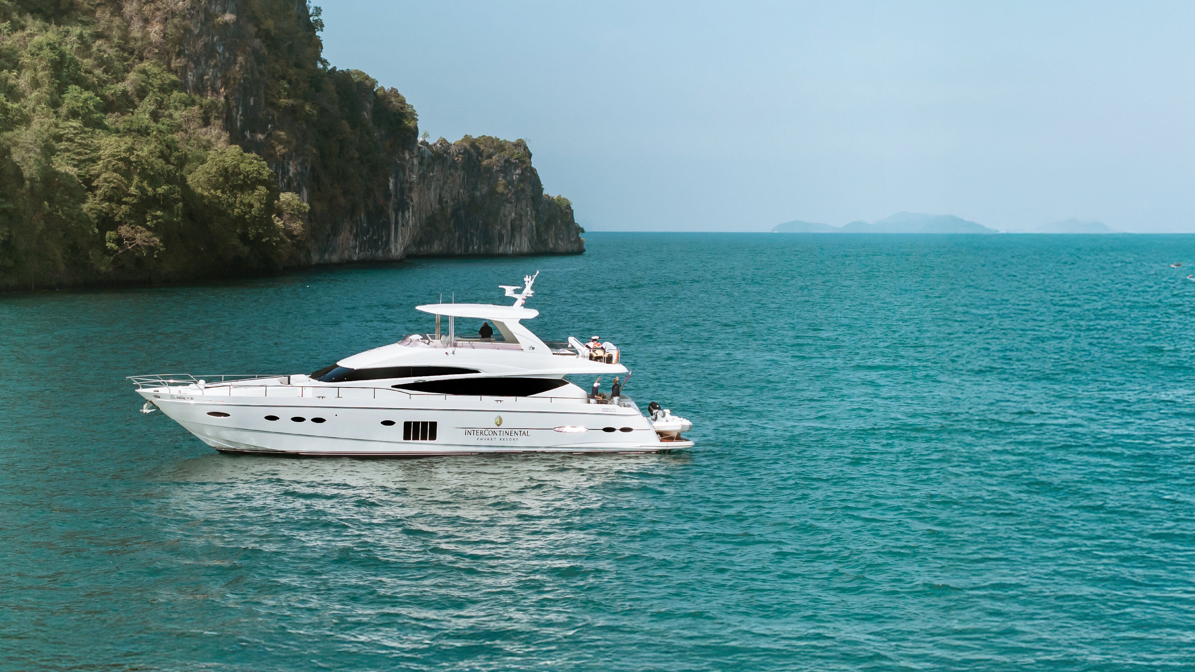 A large yacht named 'INTERCONTINENTAL' anchored near a rocky coastline with clear turquoise water.