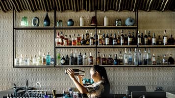 A bar area with shelves of various liquor bottles, a bartender preparing a drink, and a unique ceiling design.