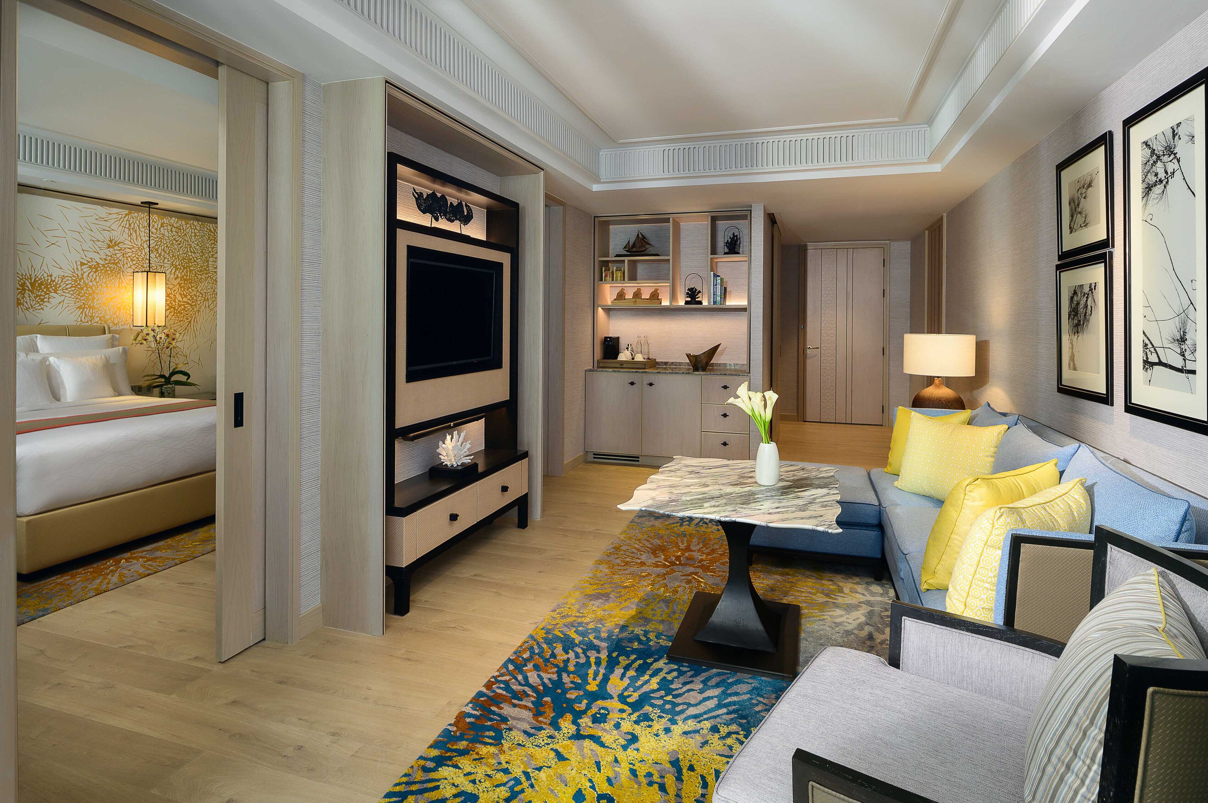 A hotel room with a bed, a TV, a sofa, a coffee table, and a kitchen area.