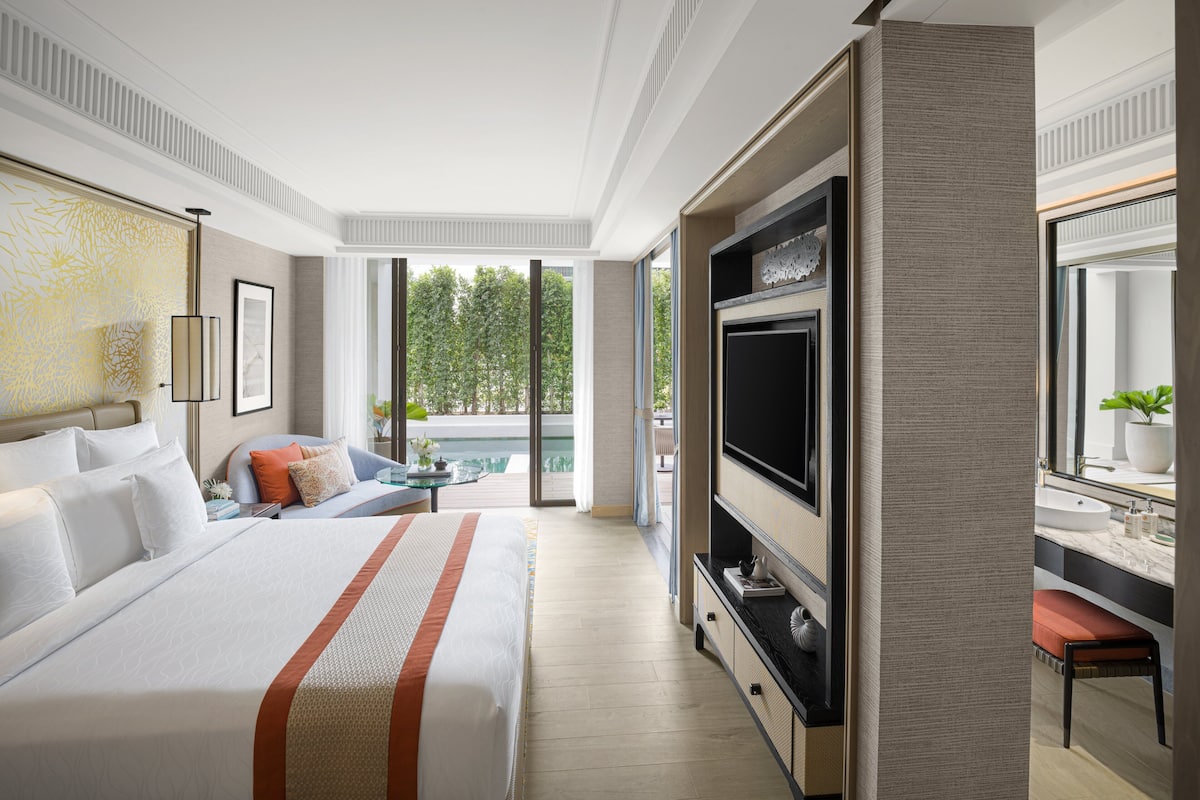 Een moderne hotelkamer met een groot bed, een televisie en een balkon met uitzicht op het zwembad.