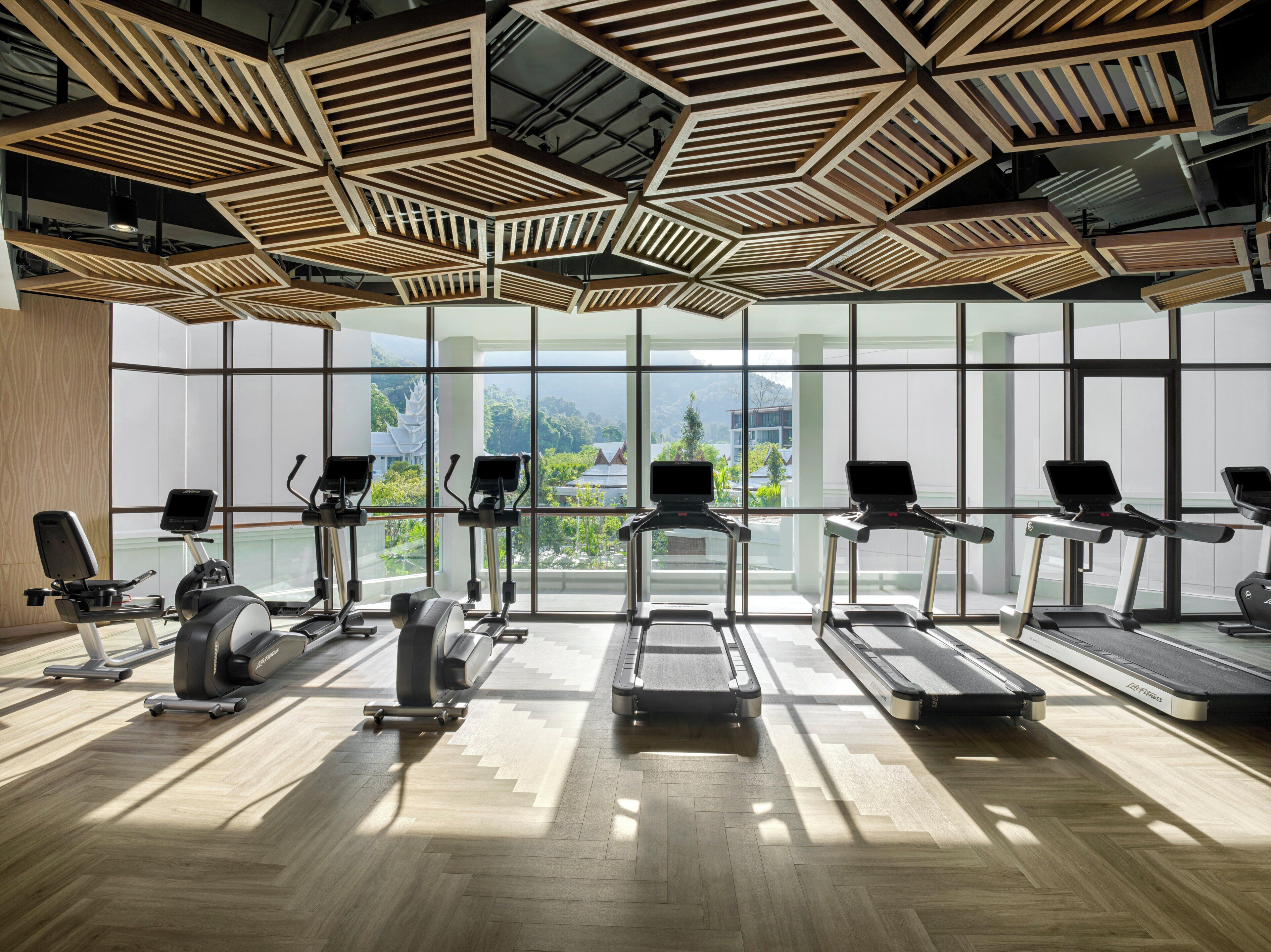 A gym with exercise equipment, large windows, and a wooden ceiling design.