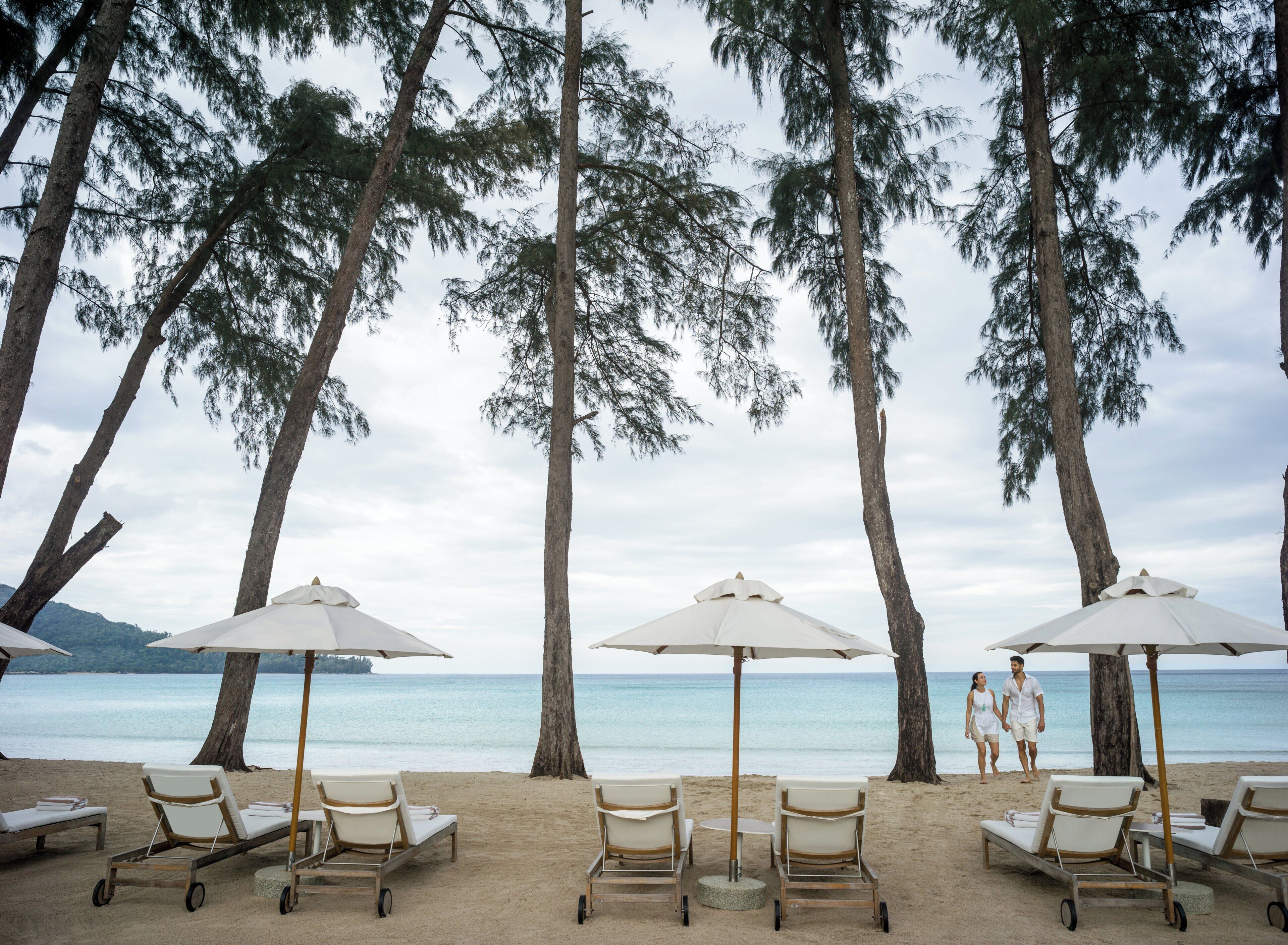 A beach with lounge chairs and umbrellas, trees, and a view of the sea.