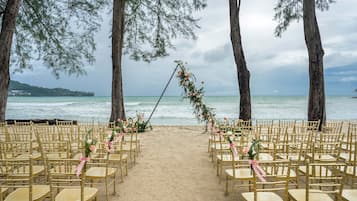A beach wedding setup with rows of gold chairs and a floral arch.