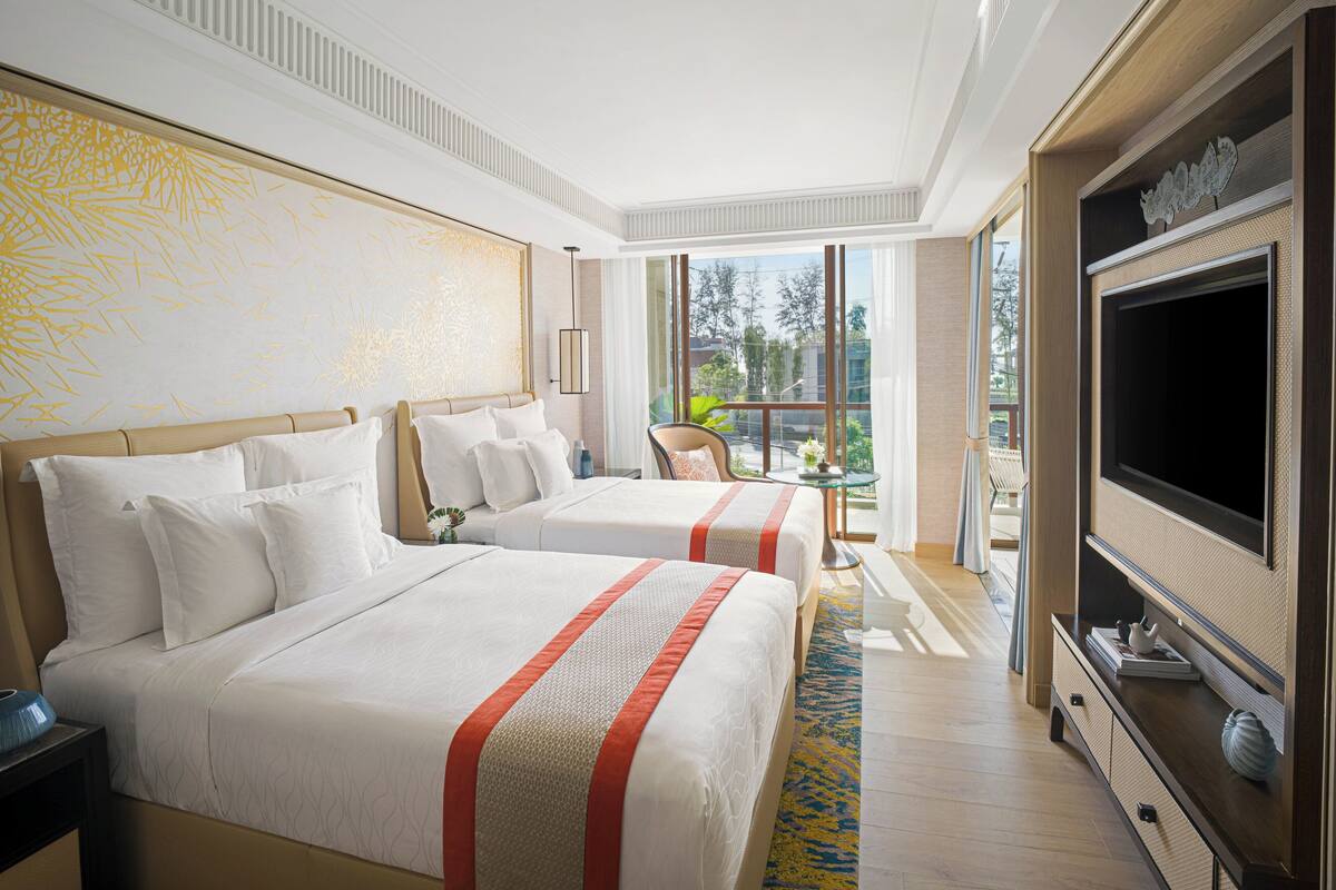 Een hotelkamer met twee bedden, een televisie, een balkon met uitzicht en een groot raam.