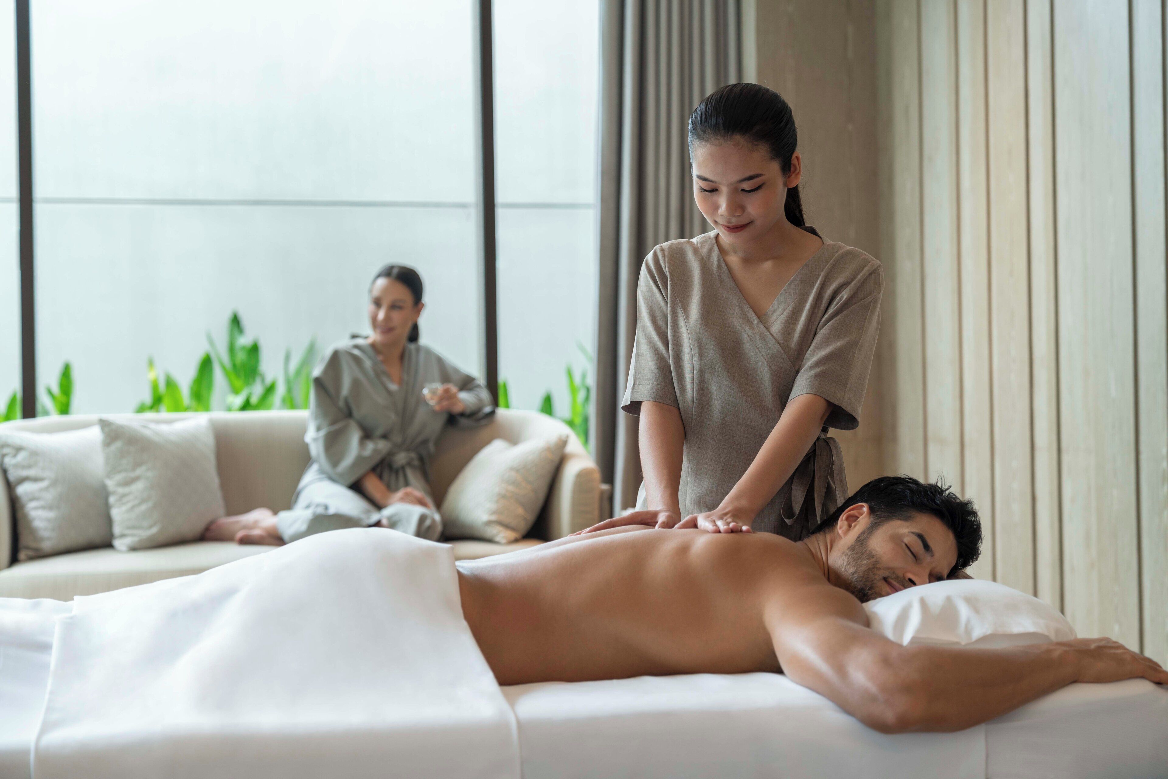 A massage therapy session in a room with a sofa and a massage table.
