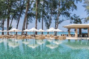 An infinity pool with clear water, surrounded by lounge chairs and umbrellas, with a view of the ocean and tall trees in the background. - InterContinental Phuket Resort by IHG (Kamala)