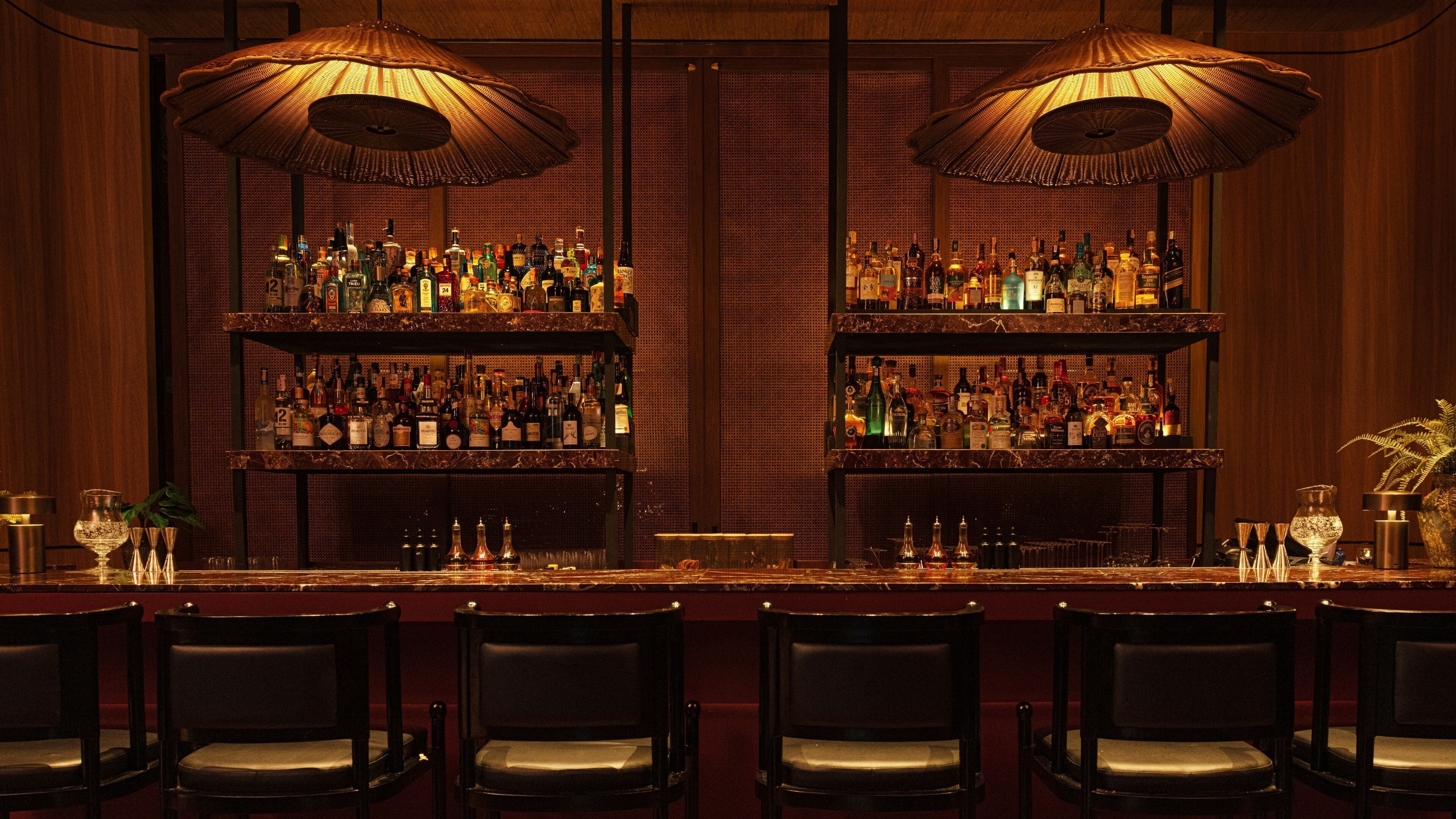 A bar area with two shelves of liquor bottles, a long counter, and six chairs.