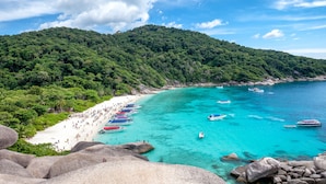 A beach with clear turquoise water, a sandy shore, and boats.