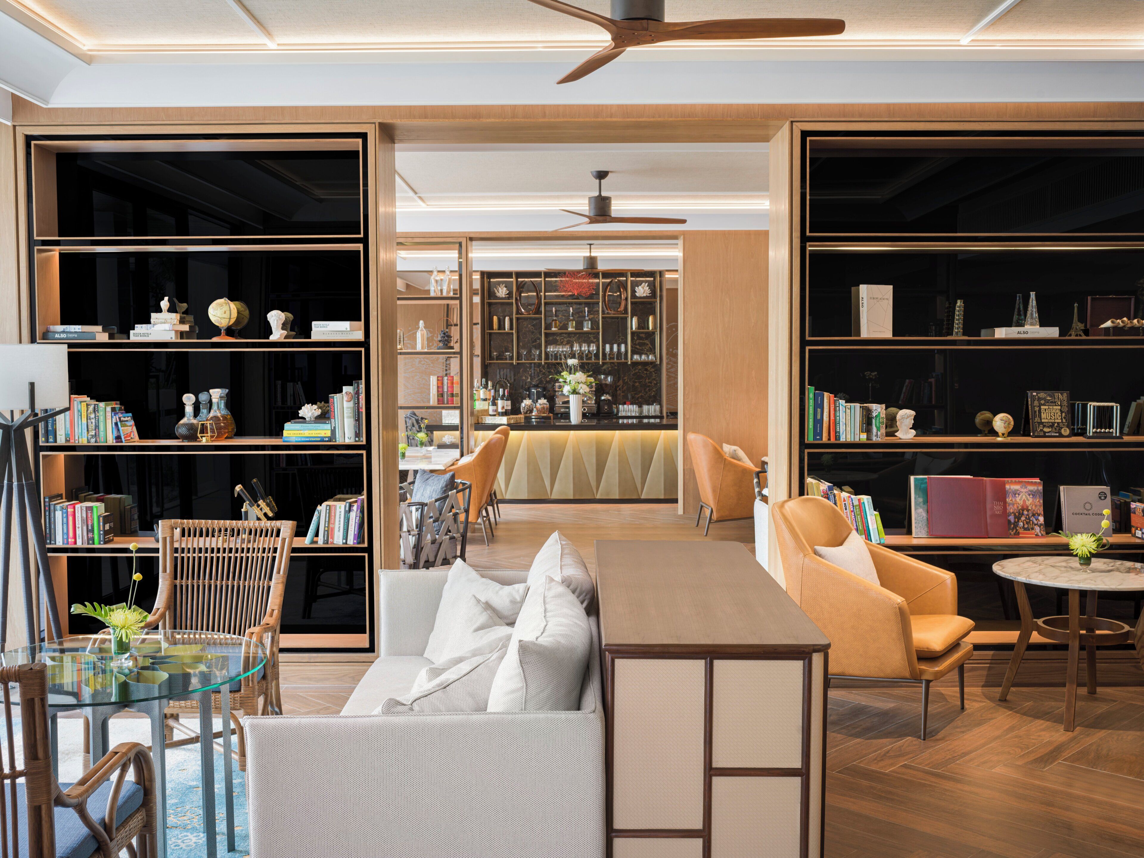 A modern living room with a glass coffee table, a sofa, and a dining area with chairs. There are bookshelves filled with books and decorative items.