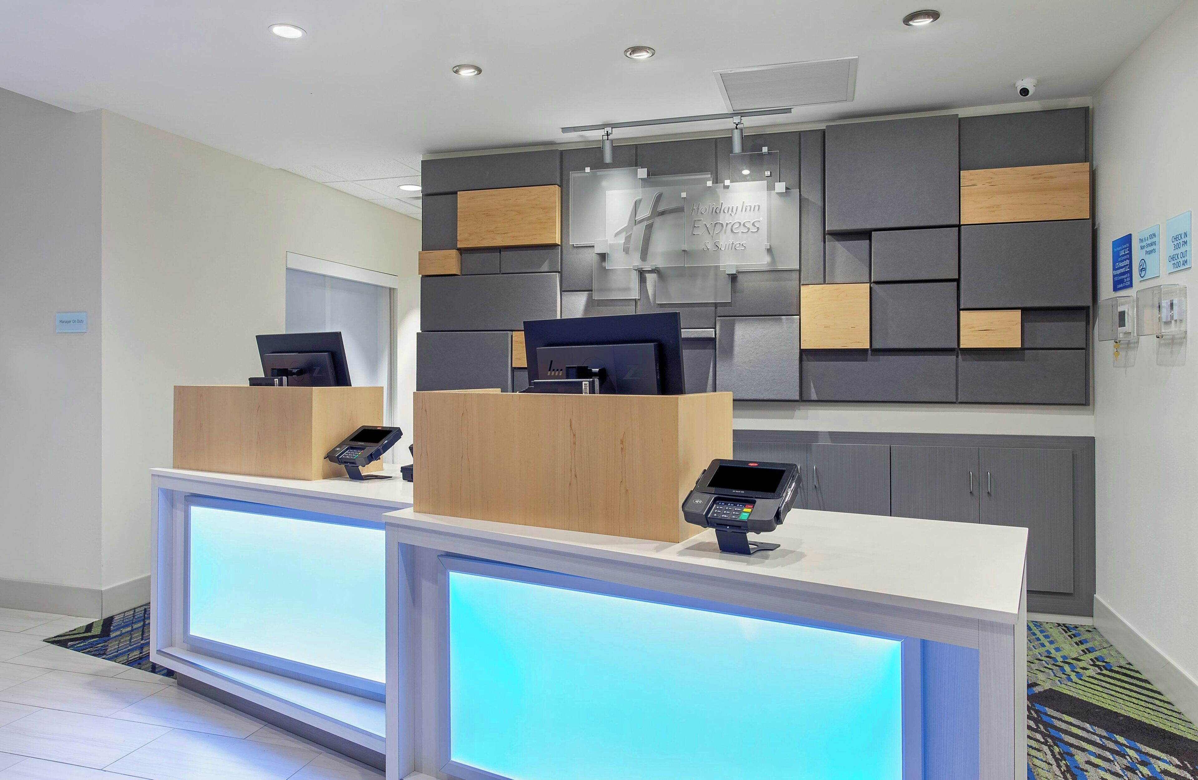A hotel reception area with two reception desks, a modern wall design, and a visible sign for Holiday Inn Express & Suites.