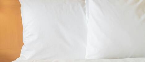 A bed with white bedding and pillows against a wooden headboard.