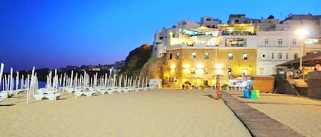 A beachside hotel with a prominent cliffside view, a sandy beach, and a wooden boardwalk.