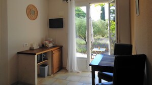 A compact room with a kitchenette, a dining area with a table and chairs, a television mounted on the wall, and a view of the outdoors through a door.