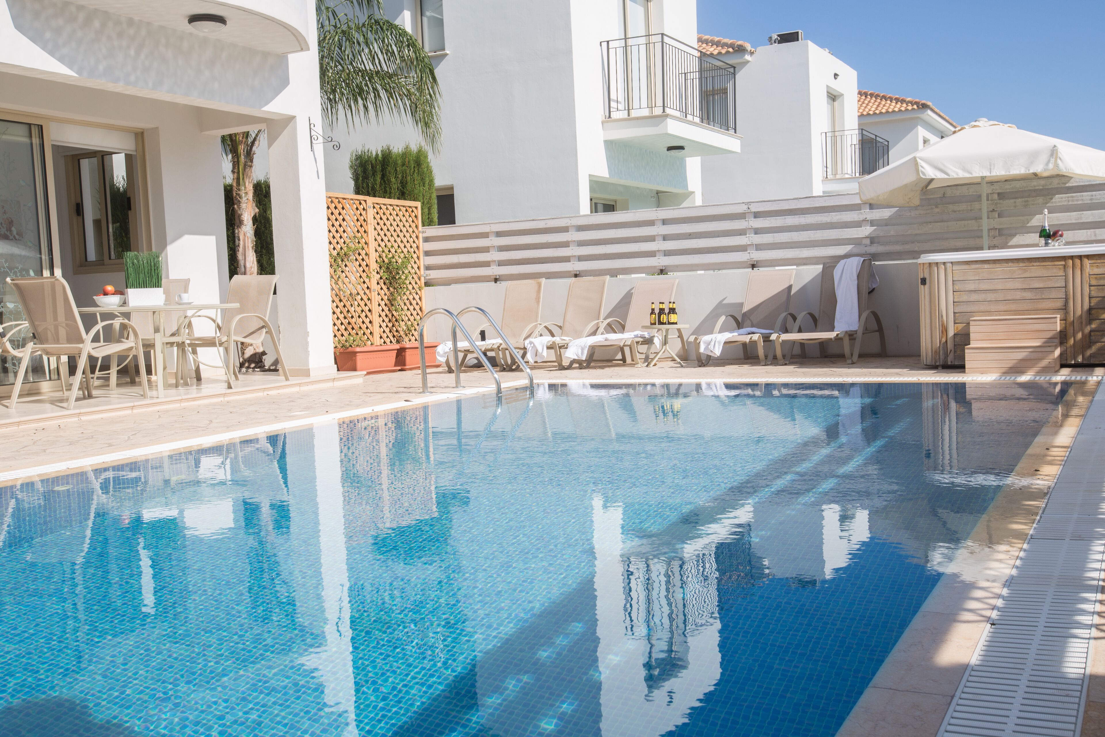 Piscina com espreguiçadeiras e uma mesa, rodeada por um edifício branco com varandas.