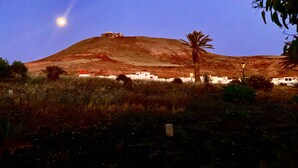 A hill with a building at the top, surrounded by vegetation and a clear sky.