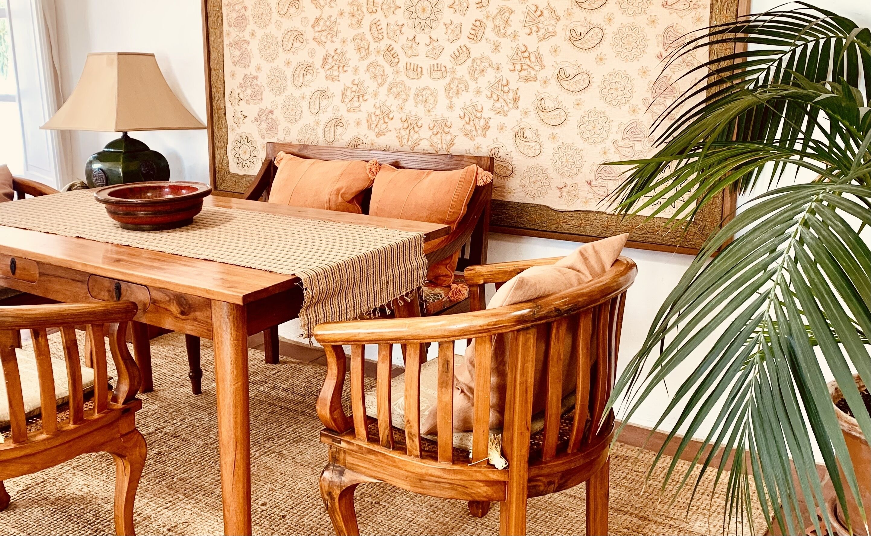 A cozy room with a wooden dining table, chairs, a sofa with cushions, a lamp, and a large plant.