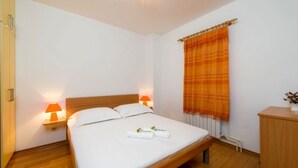 Een net opgemaakt bed met witte lakens en twee kussens, een houten hoofdbord en twee bedlampen met oranje kapjes.