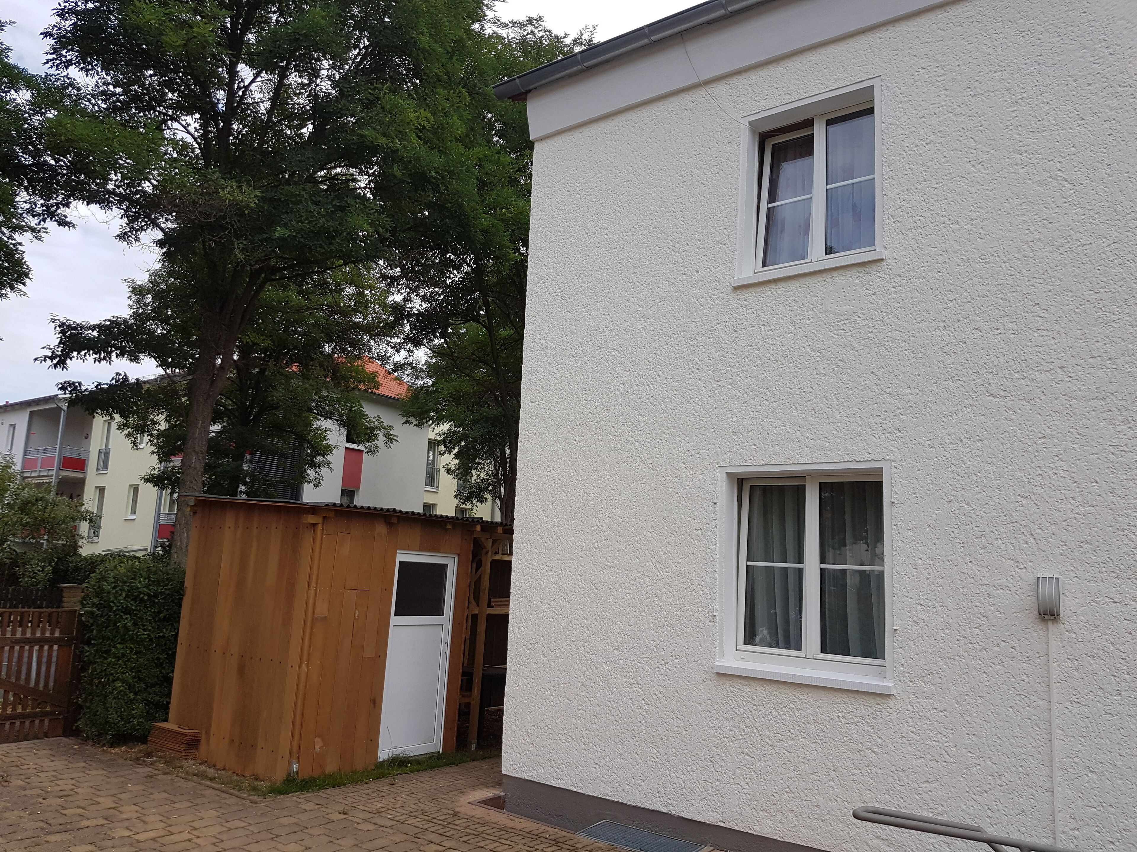 Un immeuble résidentiel de deux étages, à l’extérieur blanc, avec une clôture en bois et un arbre en arrière-plan.