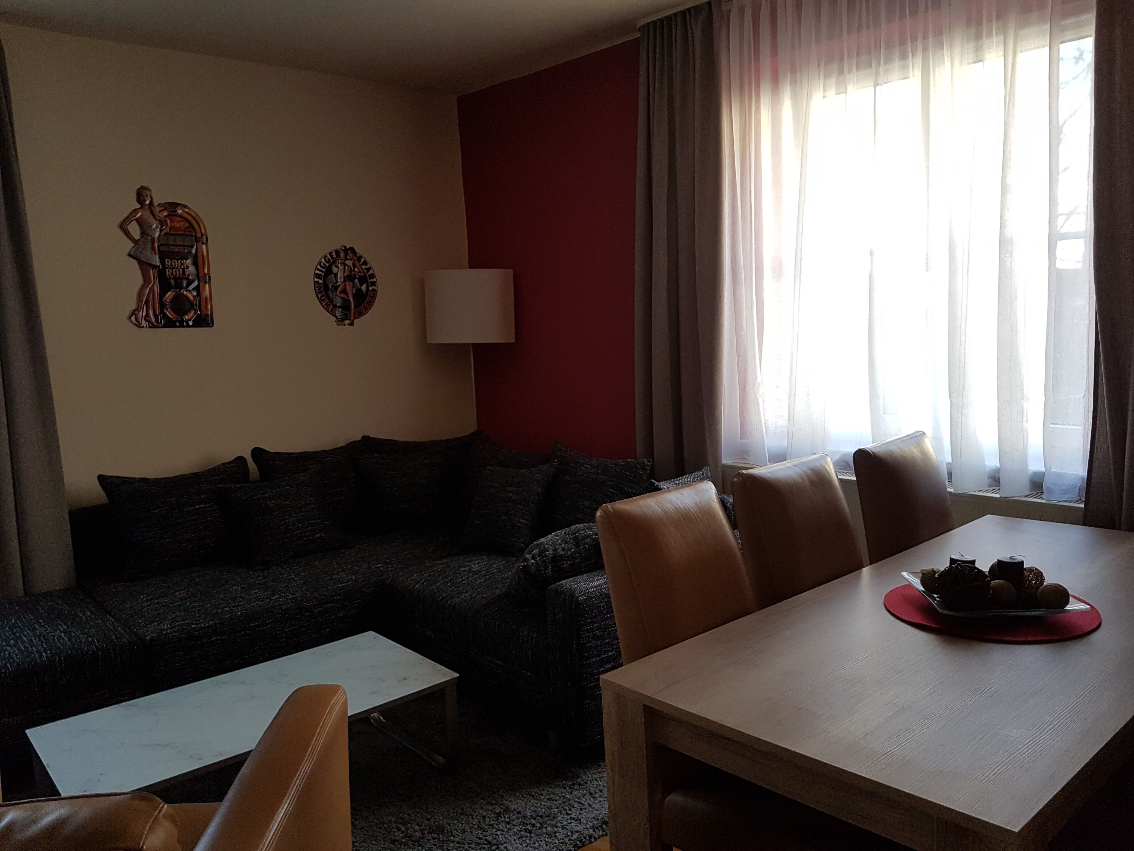 Una sala de estar con un sofá, una mesa de comedor con sillas, una lámpara y una ventana con cortinas.