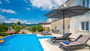 A swimming pool with lounge chairs and umbrellas, surrounded by a building with a white exterior and a view of mountains. - Wonderful private villa for 10 people with A/C, private pool, WIFI, TV and terrace (Novi Vinodolski)