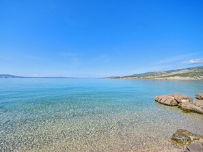 Una vista limpida su un mare calmo, con coste rocciose e colline lontane sotto un cielo azzurro.