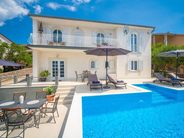 A two-story house with a swimming pool, outdoor seating, and a balcony.
