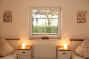 A room with two bedside tables, a window with a view of a house and tree, and two wall-mounted flower market posters.