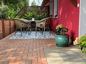 A patio with a brick floor, a checkered rug, wicker chairs, and a potted plant.
