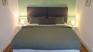 A neatly made bed with a green bedspread and two pillows, flanked by bedside lamps on a white nightstand. - Apartment Annette Mieth - Apartment (Weitenhagen)