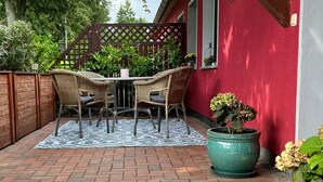 A patio with a brick floor, a checkered rug, wicker chairs, and a potted plant. - Apartment Annette Mieth - Apartment (Weitenhagen)