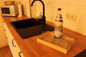 A kitchen with a black sink, a microwave, a bottle of water, and a tray with two glasses.