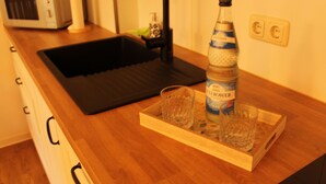 A kitchen with a black sink, a microwave, a bottle of water, and a tray with two glasses. - Apartment Annette Mieth - Apartment (Weitenhagen)