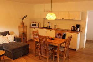 A compact living space with a kitchenette, a dining area with wooden chairs, a sofa, and a small side table.