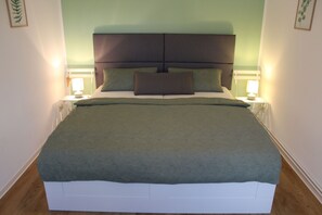 A neatly made bed with a green bedspread and two pillows, flanked by bedside lamps on a white nightstand.