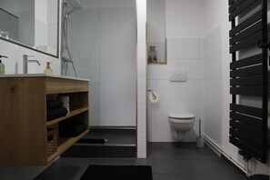 Un baño moderno con un mueble de tocador de madera, inodoro y ducha.