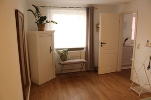 A room with a wooden floor, a white radiator, a bench with a cushion, a potted plant, and a white door.