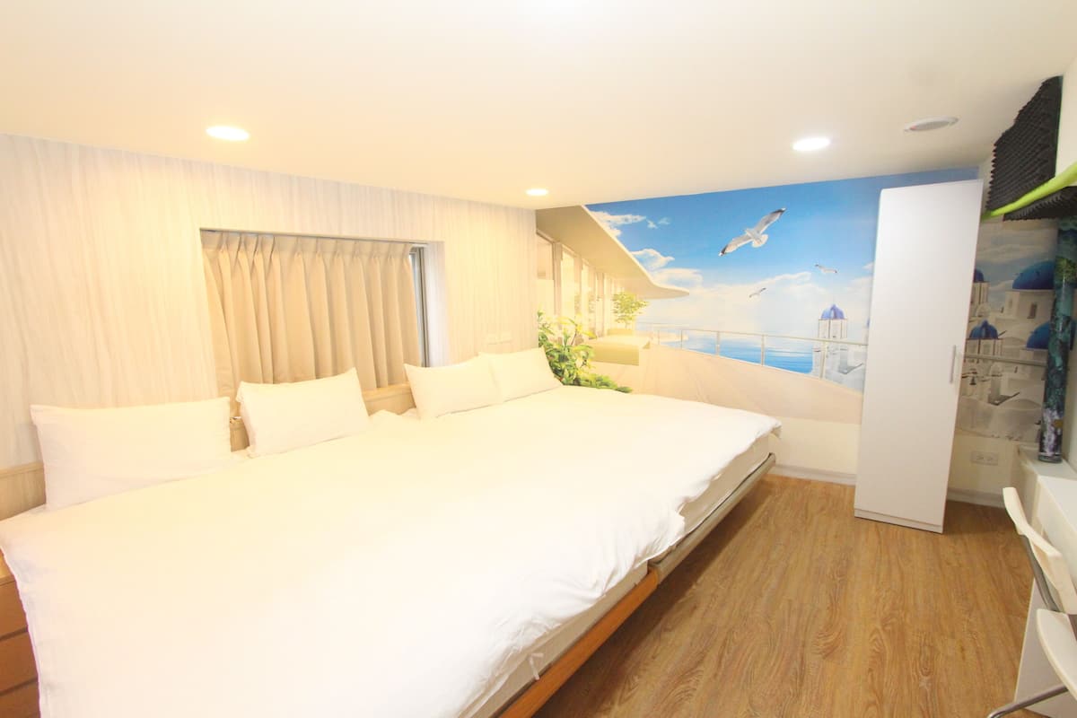 A hotel room with a large bed, a view of the sea, and a mural of seagulls.