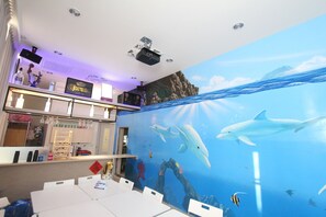 A room with a large mural of marine life, a bar area with shelves of bottles, and a projector on the ceiling. - HF Keelung (Keelung)