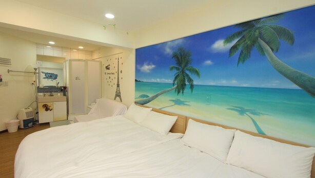 Een slaapkamer met een groot bed, een schilderij van een strand en een badkamer die door een open deur zichtbaar is.