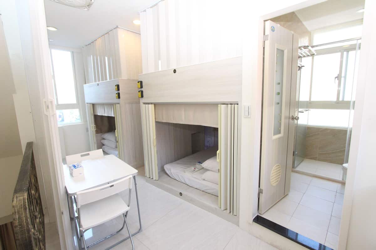 A compact room with bunk beds, a small table, and a shower area.