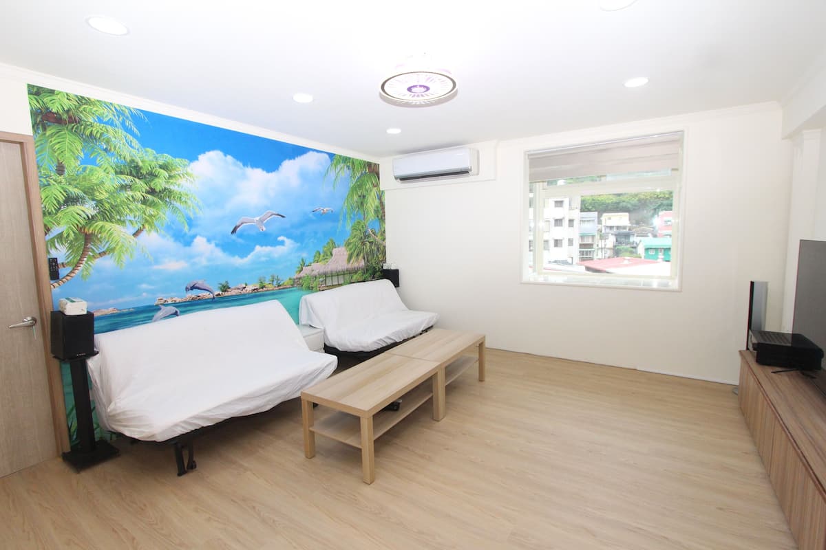 A room with a mural of a beach scene, a bed with white bedding, a wooden bench, and a TV on a wooden cabinet.
