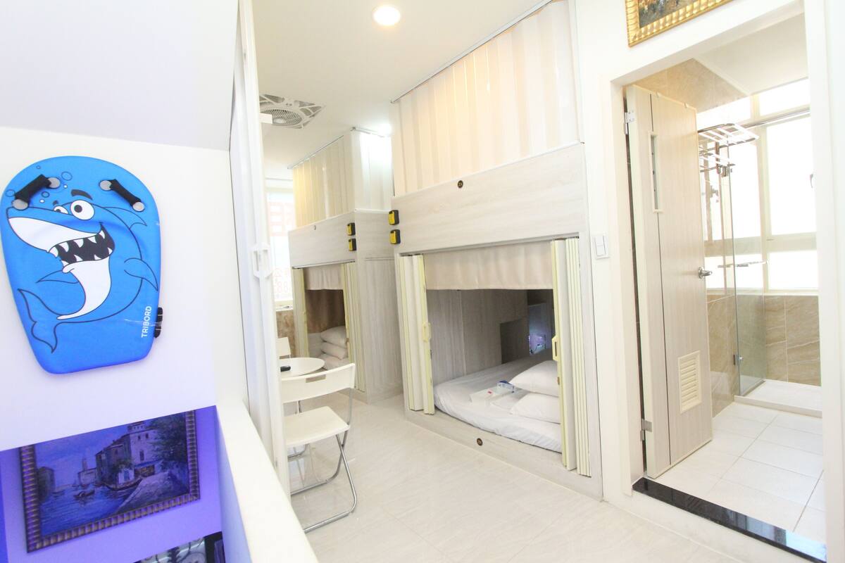 A hotel room with bunk beds, a small desk, and a bathroom with a glass shower.