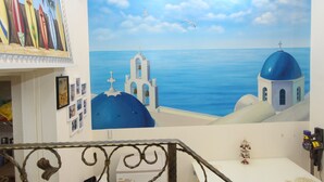 Een kamer met een groot muurschildering van een kustlandschap, met daarin een kerk en uitzicht op zee.