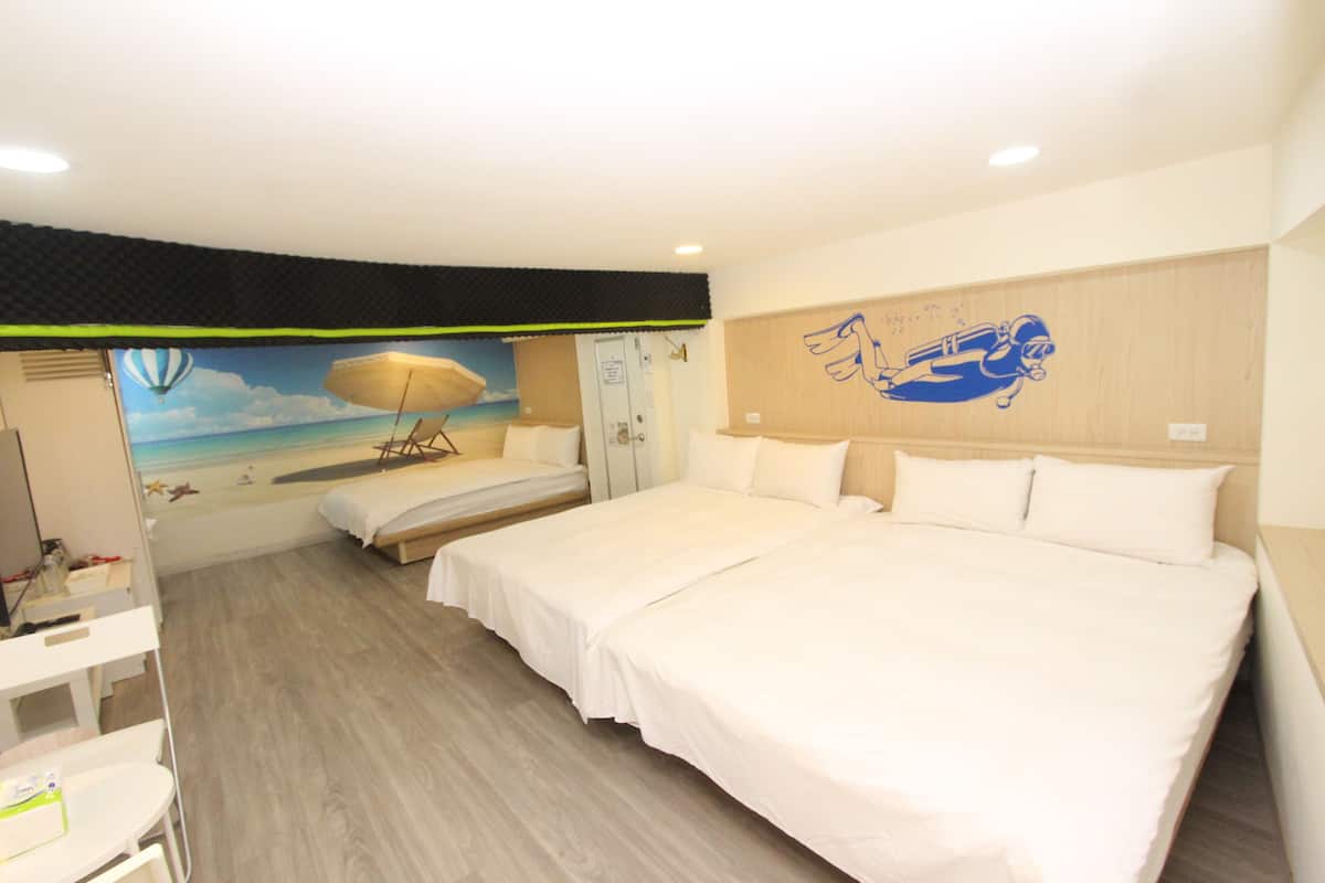 A hotel room with a large bed, a desk, and a chair. There is a mural of a beach scene on the wall.