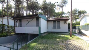 A small, single-story building with a green roof and white walls, surrounded by a paved area with a patterned design. - Villa just a few steps from the beach (Lignano Sabbiadoro)