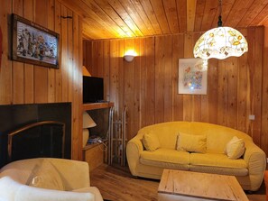 A cozy room with wooden walls, a yellow sofa, a television, and a fireplace. - Chalet-style apt 4/5 pers, center of resort, 50m from slopes (Pra-Loup)