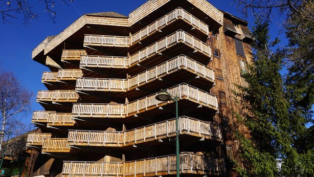 A multi-story wooden building with balconies, likely a hotel or residential complex. - Chalet-style apt 4/5 pers, center of resort, 50m from slopes (Pra-Loup)