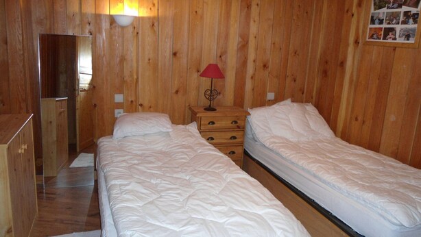 A wooden-paneled room with two beds, a nightstand with a lamp, and a dresser.